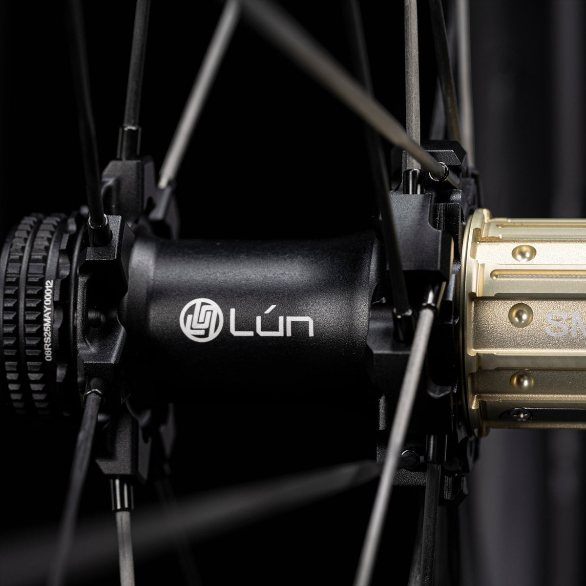 NorVelo Lún Route 3 road bike wheel hub with black carbon spokes and gold-toned cassette body on a black background