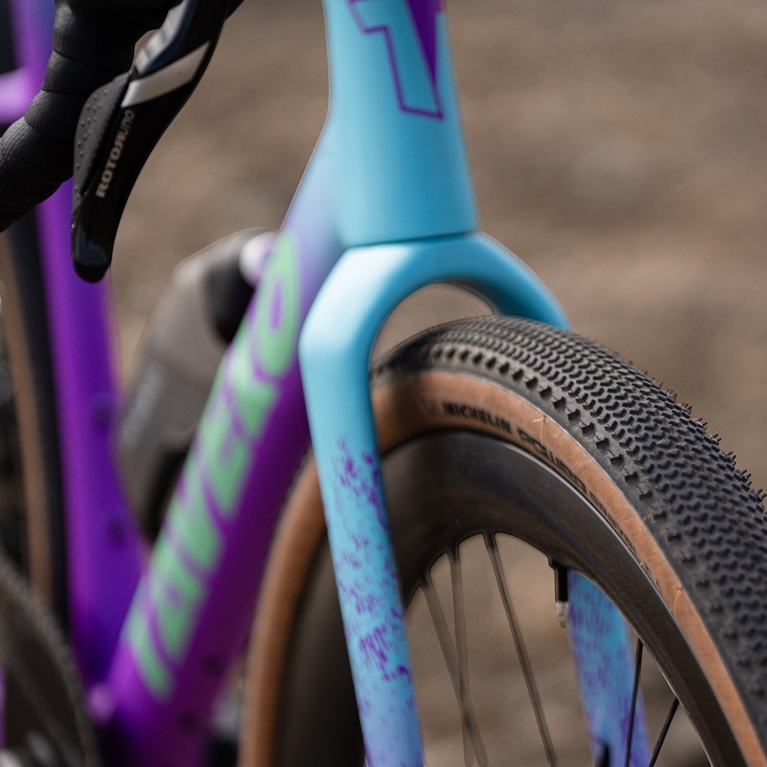 NorVelo Tavelo Grow aero gravel bike frame in blue and purple gradient with tan wall tires on a gravel path