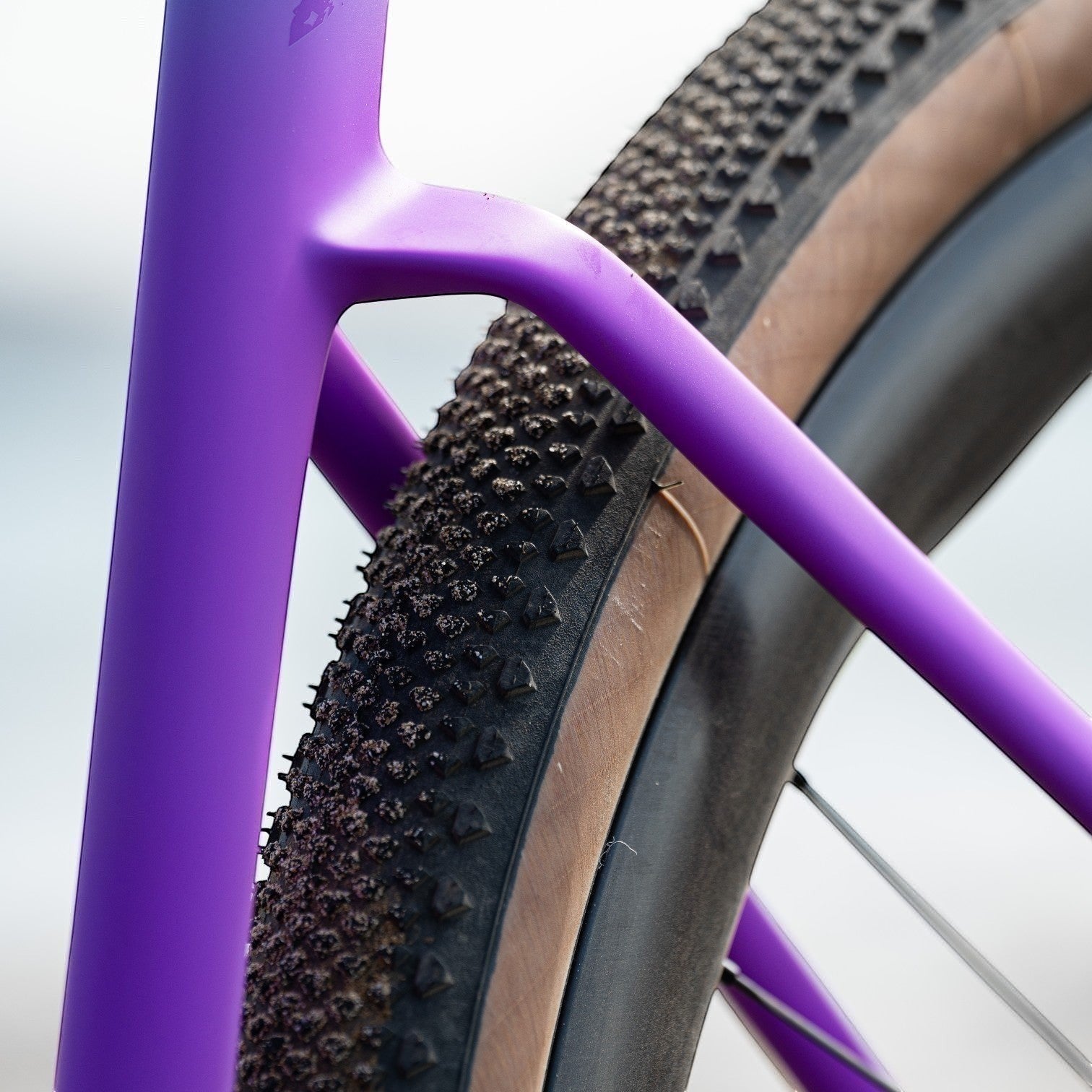 NorVelo Tavelo Grow aero-gravel bike frame in vibrant purple with tan wall gravel tires and carbon seat stay detail.